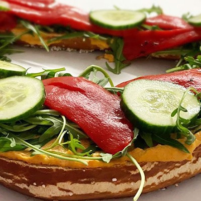 Vegane Riesenbreze mit verschiedenen Sorten Hummus, gegrilltem Gemüse, Rucola-Salat